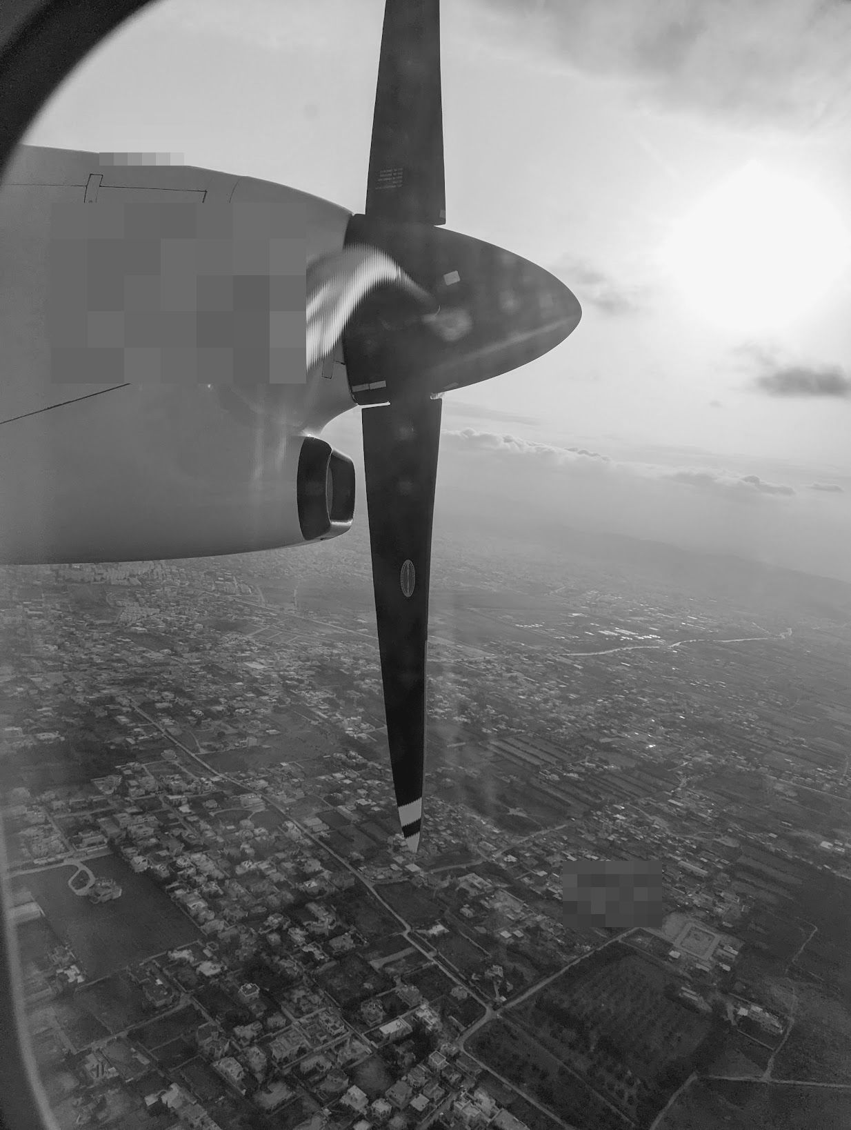 A turboprop wing and propeller over a city on approach.