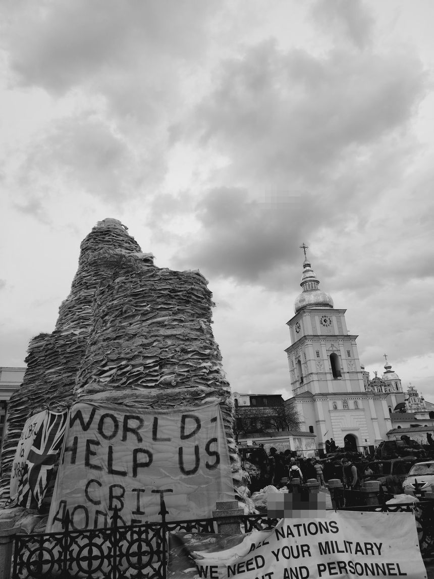 A monument encased in sandbags, a cathedral behind it.